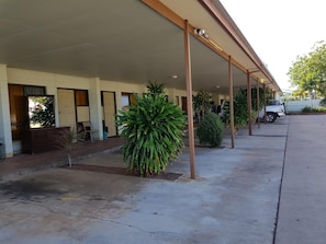 A covered outdoor area with a concrete floor, a parked white truck, and several potted plants.