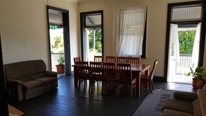 A spacious living area with a wooden dining table and chairs, a sofa, and a balcony with potted plants.