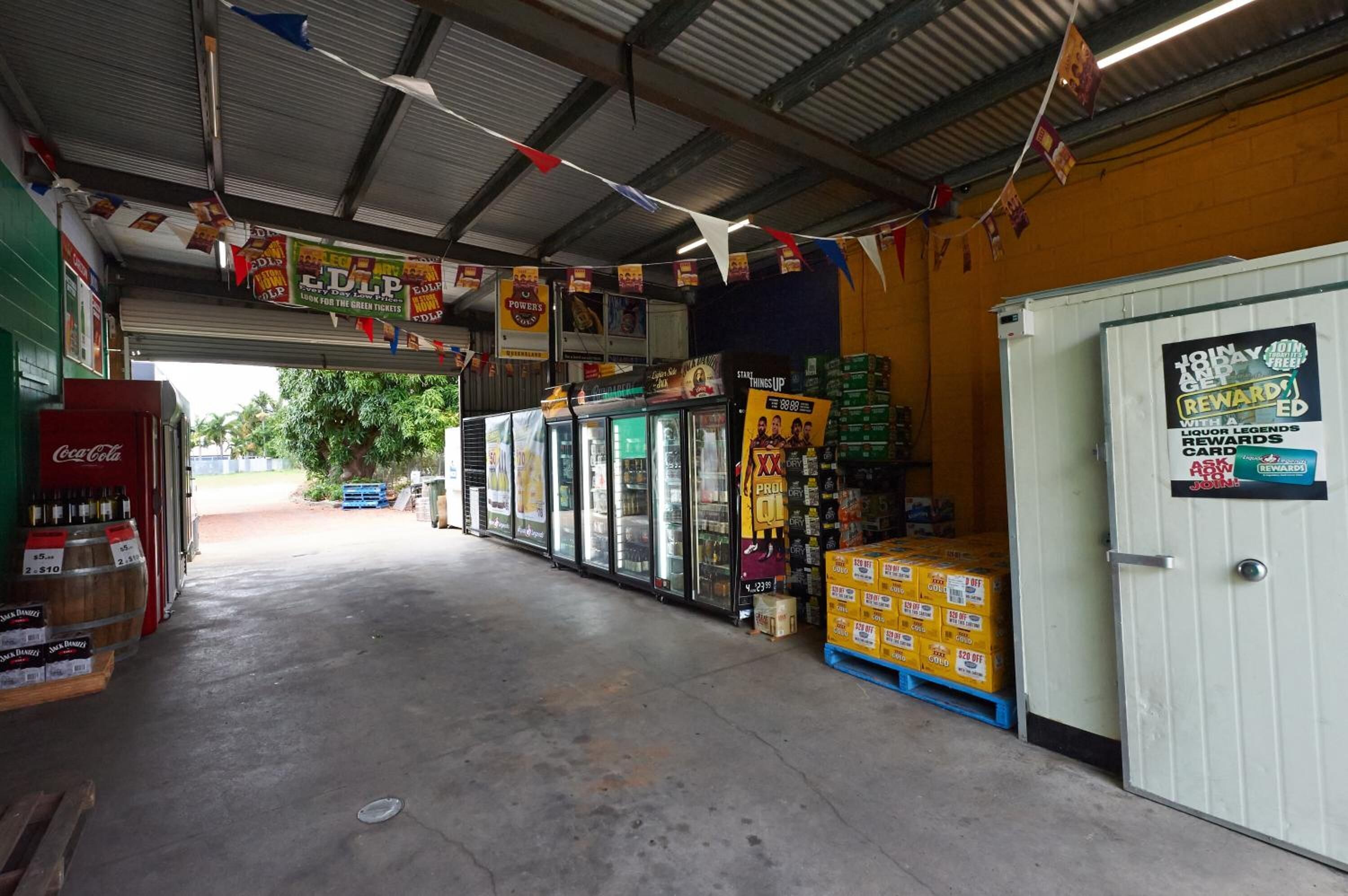 A small convenience store with a Coca-Cola cooler, refrigerated display cases, and stacked products on pallets.