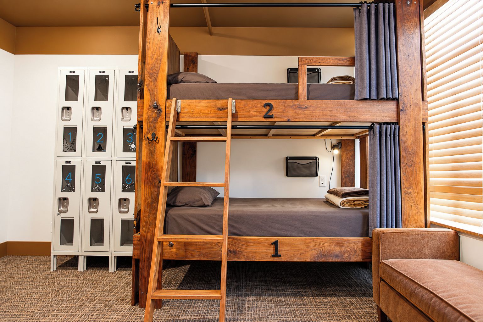 Cama litera con escalera, una mesita y un sofá en una habitación con taquillas.