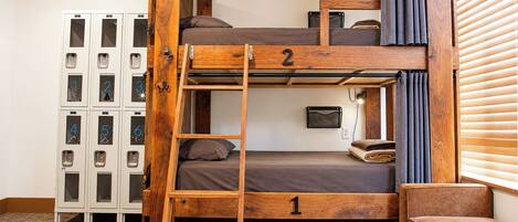 Cama litera con escalera, una mesita y un sofá en una habitación con taquillas.