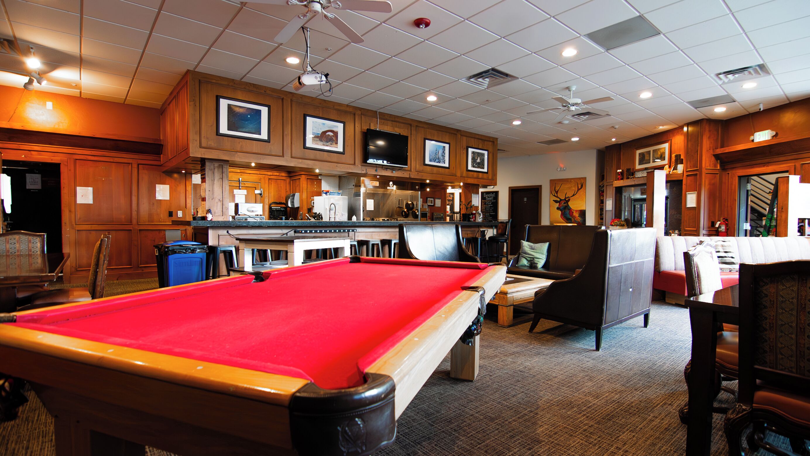 A pool table in a room with wooden paneling, a bar area, and a seating area with a fireplace.
