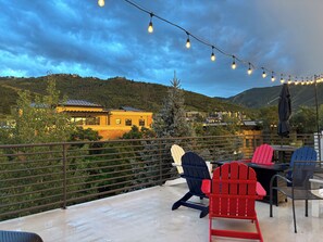 Une terrasse avec des sièges extérieurs, une vue sur une montagne et des guirlandes lumineuses.