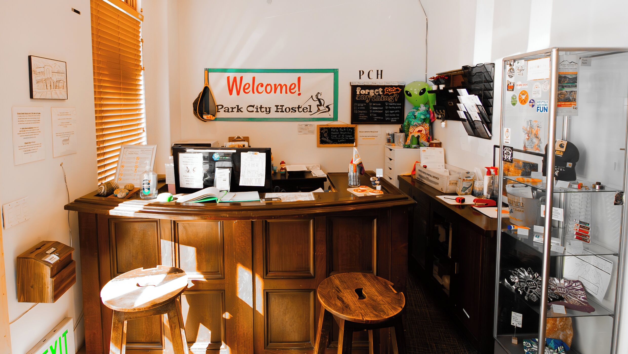 A reception desk with a 'Welcome! Park City Hostel' sign, a computer, and a bulletin board with various notices.