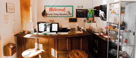A reception desk with a 'Welcome! Park City Hostel' sign, a computer, and a bulletin board with various notices.
