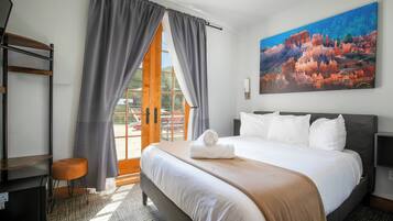 Habitación de hotel con cama, escritorio, silla, un cuadro y vistas al exterior.