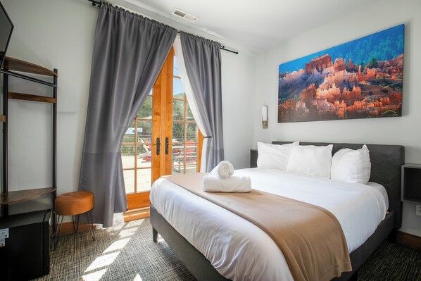 Une chambre d’hôtel avec un lit, un bureau, une chaise, un tableau et une vue sur l’extérieur.