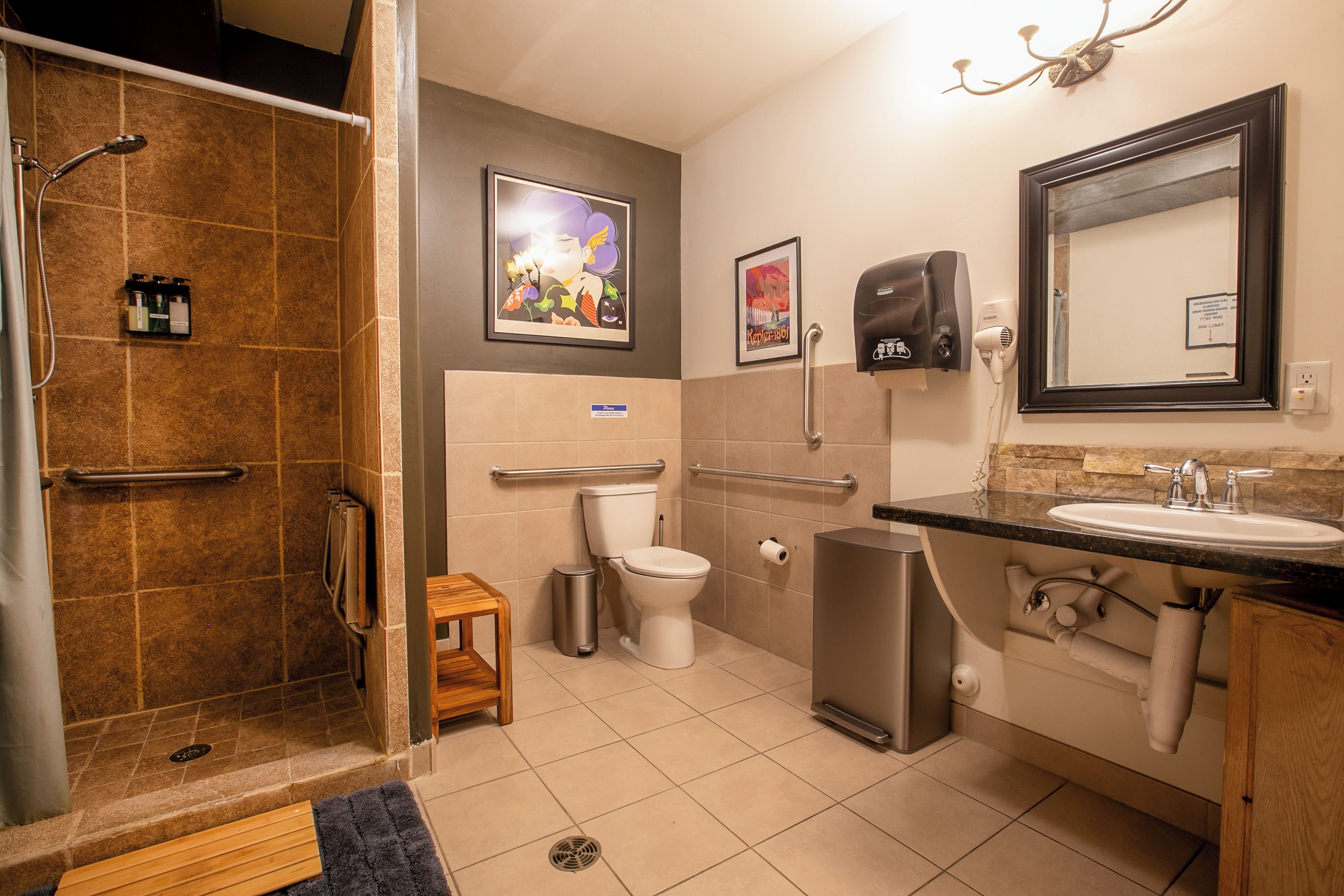 A bathroom with a shower, toilet, bidet, and sink. There are hand dryers and a trash can.