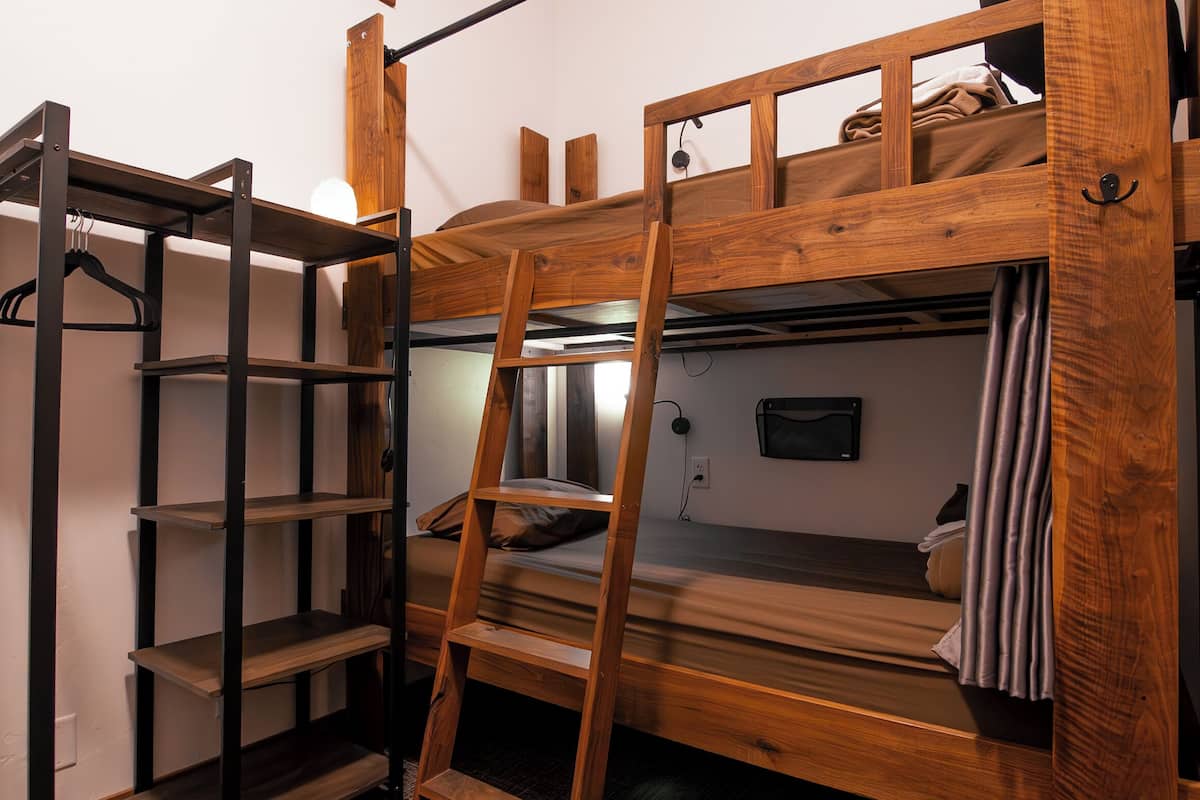 Une chambre avec un lit superposé, une échelle, des étagères et une lampe fixée au mur.