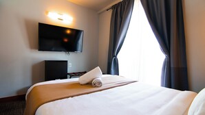 Une chambre d’hôtel avec un lit, un téléviseur à écran plat fixé au mur et une fenêtre avec des rideaux.