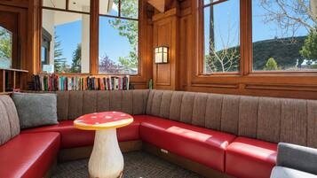 Un coin lecture confortable avec un banc rembourré de couleur rouge, une table en bois ornée d’un motif en forme de champignon et une bibliothèque remplie de livres.