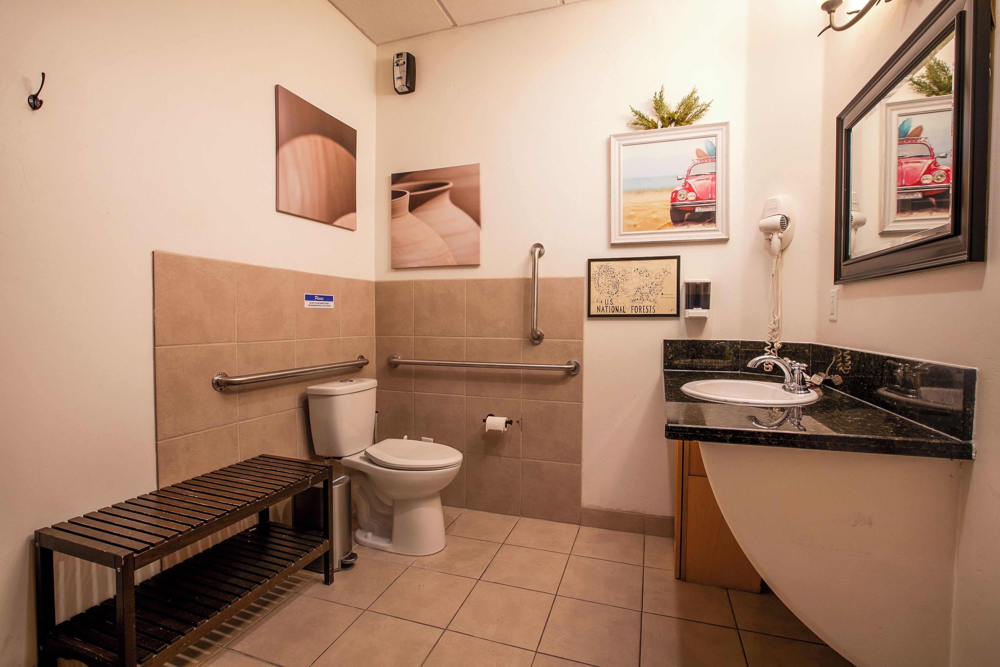 Une salle de bain équipée de toilettes, de barres d’appui, d’un lavabo et d’un banc.