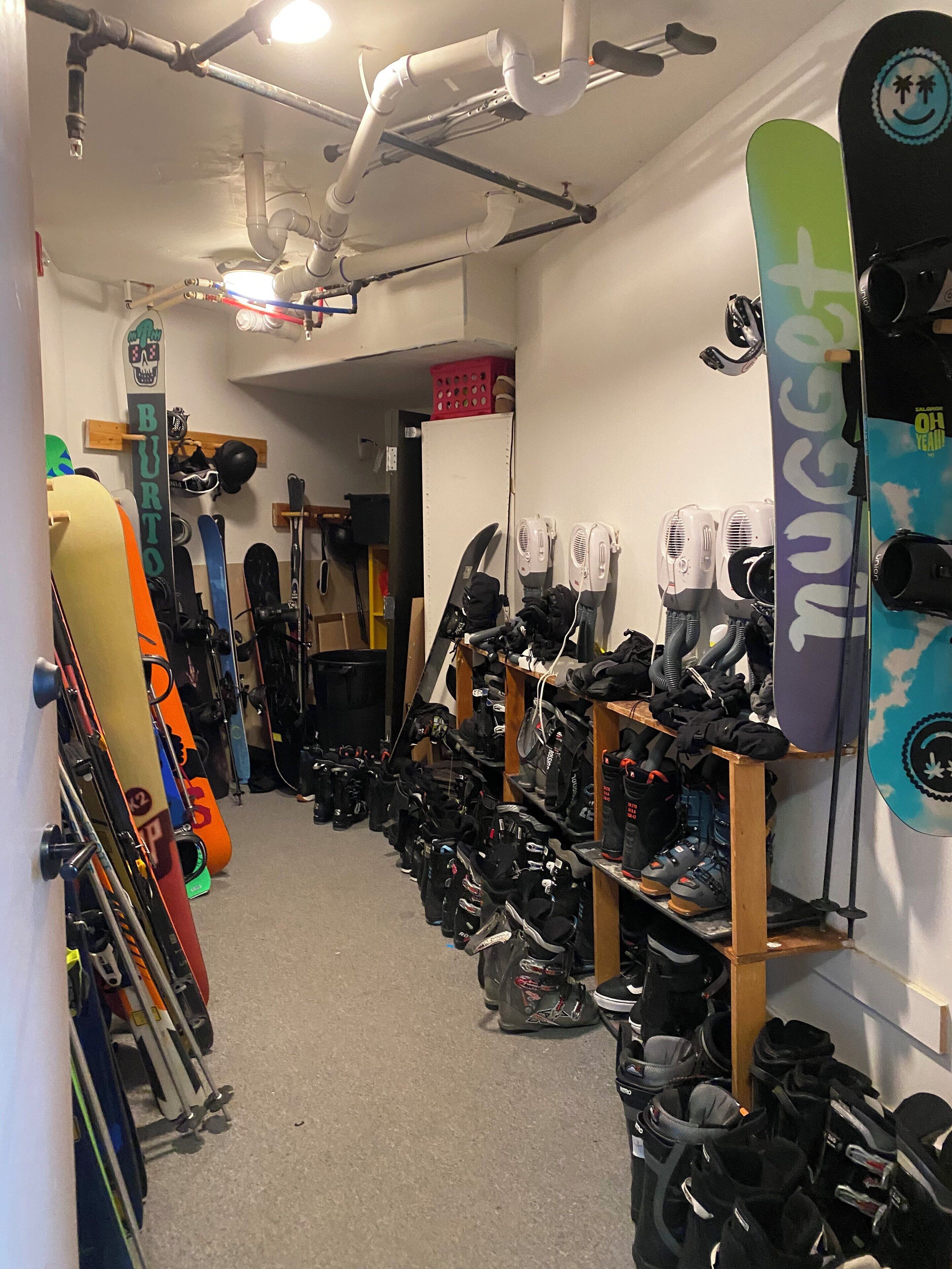 Un cuarto para guardar esquíes con esquíes y tablas de snowboard en estantes y repisas, y diverso equipo de esquí en el suelo.