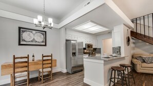 A modern kitchen with a central island, stainless steel appliances, and a dining area with wooden chairs. - South Austin Creekside Retreat!  (Austin)