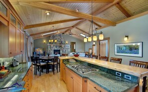 A spacious kitchen with a large island, wooden cabinets, and a stone fireplace.