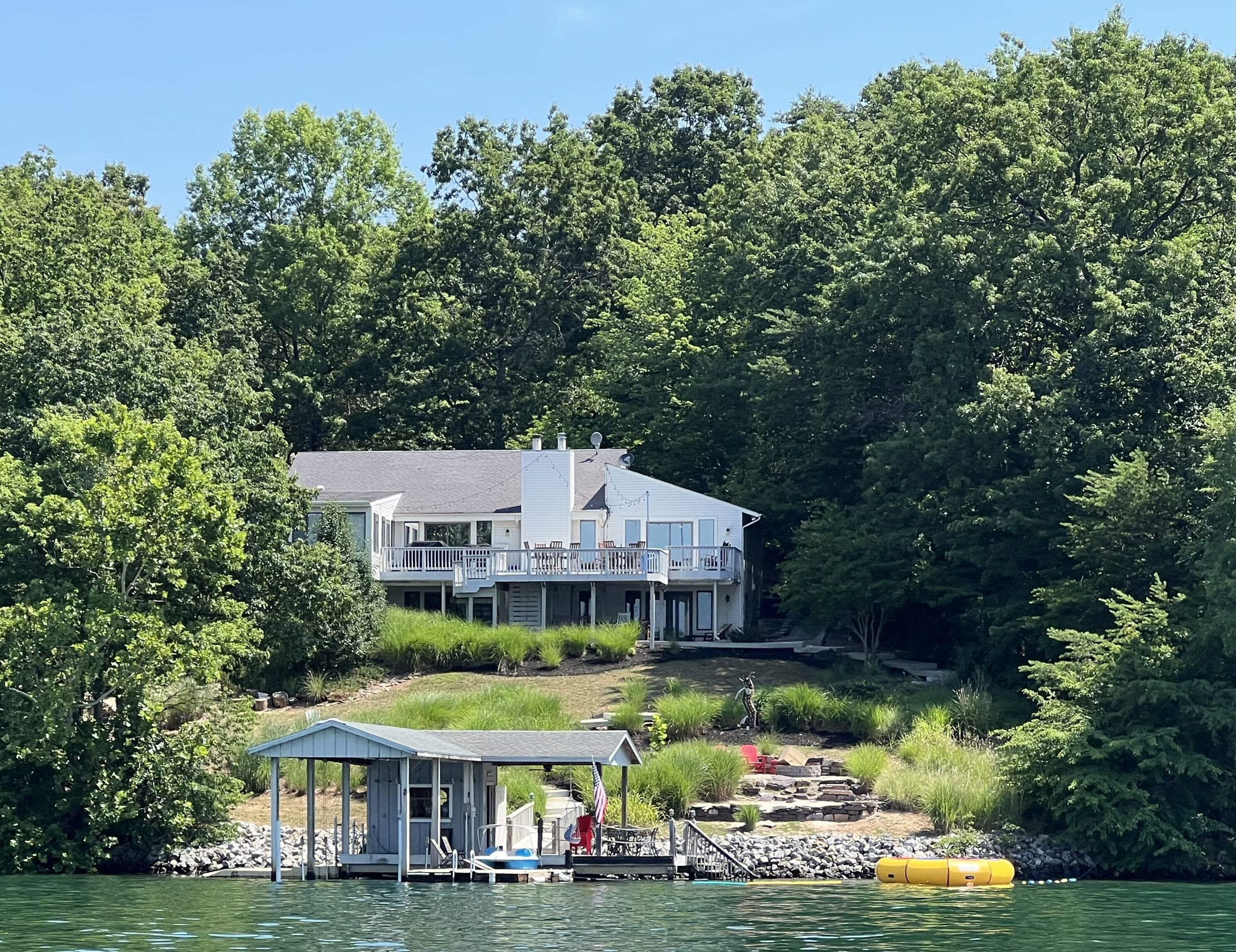 Une maison au bord du lac, dotée d’un quai, d’un abri à bateaux et d’une petite terrasse ornée d’une statue.