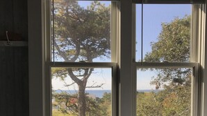 A room with a bed and a window with a view of trees and a body of water. - Provincetown: Water view, 3 BR House, Parking, Free Wifi, outdoor shower, beach! (Provincetown)