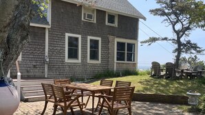 A house with a brick exterior, a patio with wooden furniture, and a view of the sky. - Provincetown: Water view, 3 BR House, Parking, Free Wifi, outdoor shower, beach! (Provincetown)