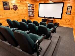 A cozy movie theater with rows of green seats, a large screen, and a collection of DVDs on shelves.