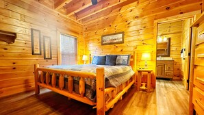 Camera da letto in una baita di legno, con un letto, lampade sui comodini, uno specchio e un piccolo bagno.