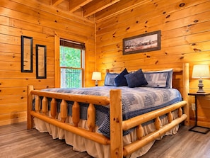 Une chambre à coucher dans une cabane en bois, avec un lit, deux lampes de chevet, une fenêtre et un tableau encadré au mur.