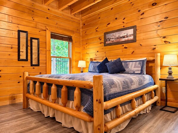 A wooden cabin bedroom with a bed, two bedside lamps, a window, and a framed picture on the wall.