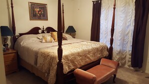 A four-poster bed with a gold and white bedspread, two bedside lamps, a wooden nightstand, a bench, and a framed floral painting on the wall. - 3 bedroom, 2 bath house. Sleeps 6. Close to 76 Hwy strip (Branson)