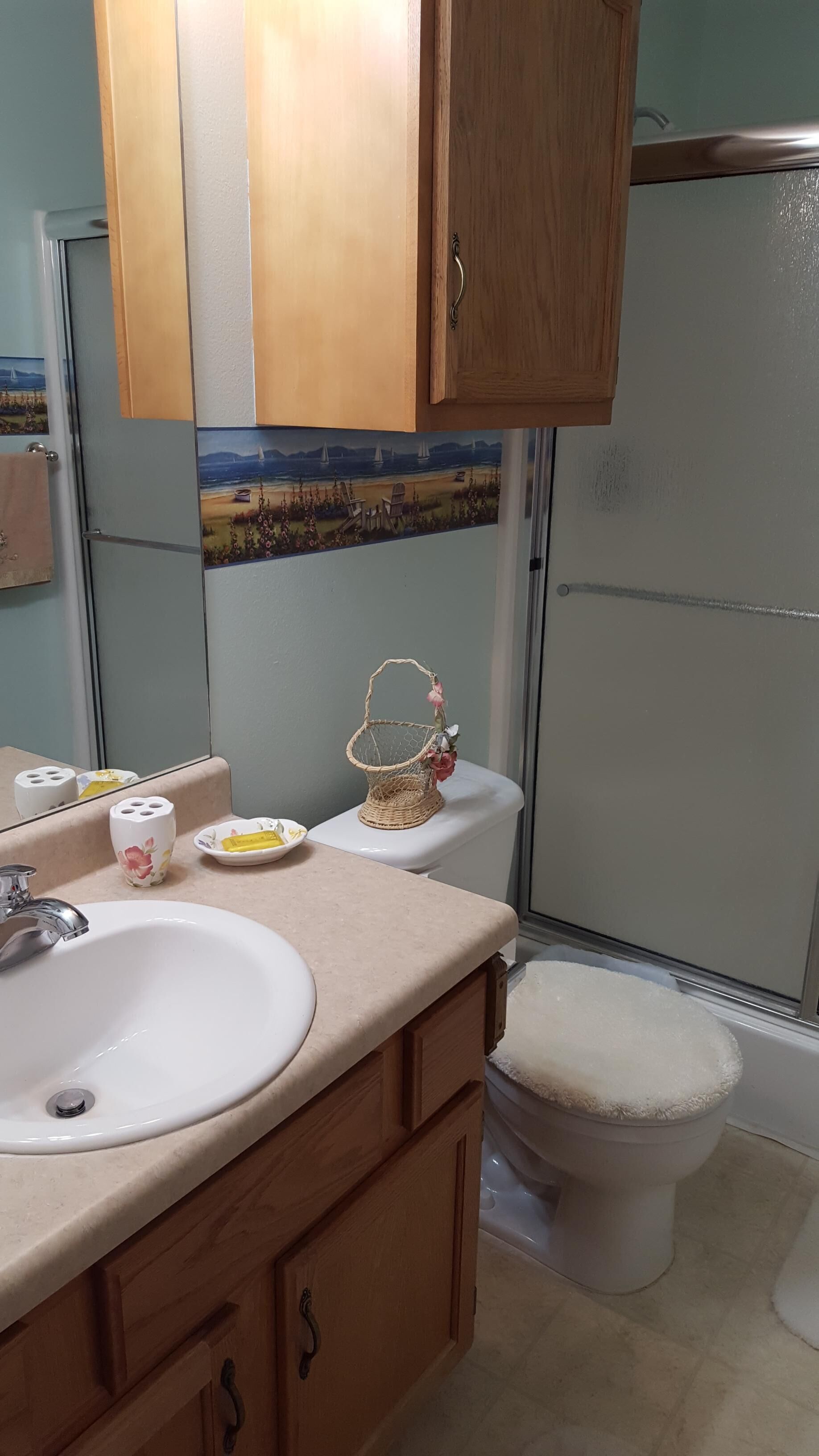 A bathroom with a white sink, wooden cabinets, a toilet, and a shower.