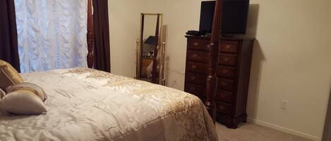A bedroom with a bed, a dresser, a mirror, and a television.