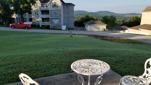 A patio with a round table and two ornate chairs, a red truck parked nearby, and a multi-story building in the background. - 3 bedroom, 2 bath house. Sleeps 6. Close to 76 Hwy strip (Branson)
