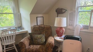 A cozy room with a patterned armchair, a small table with a lamp, a heater, and a window with a view of trees. - Cozy Country Apartment in Heart of Geauga County (Newbury)