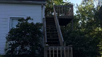 A two-story wooden deck attached to a house with a window and surrounded by greenery.