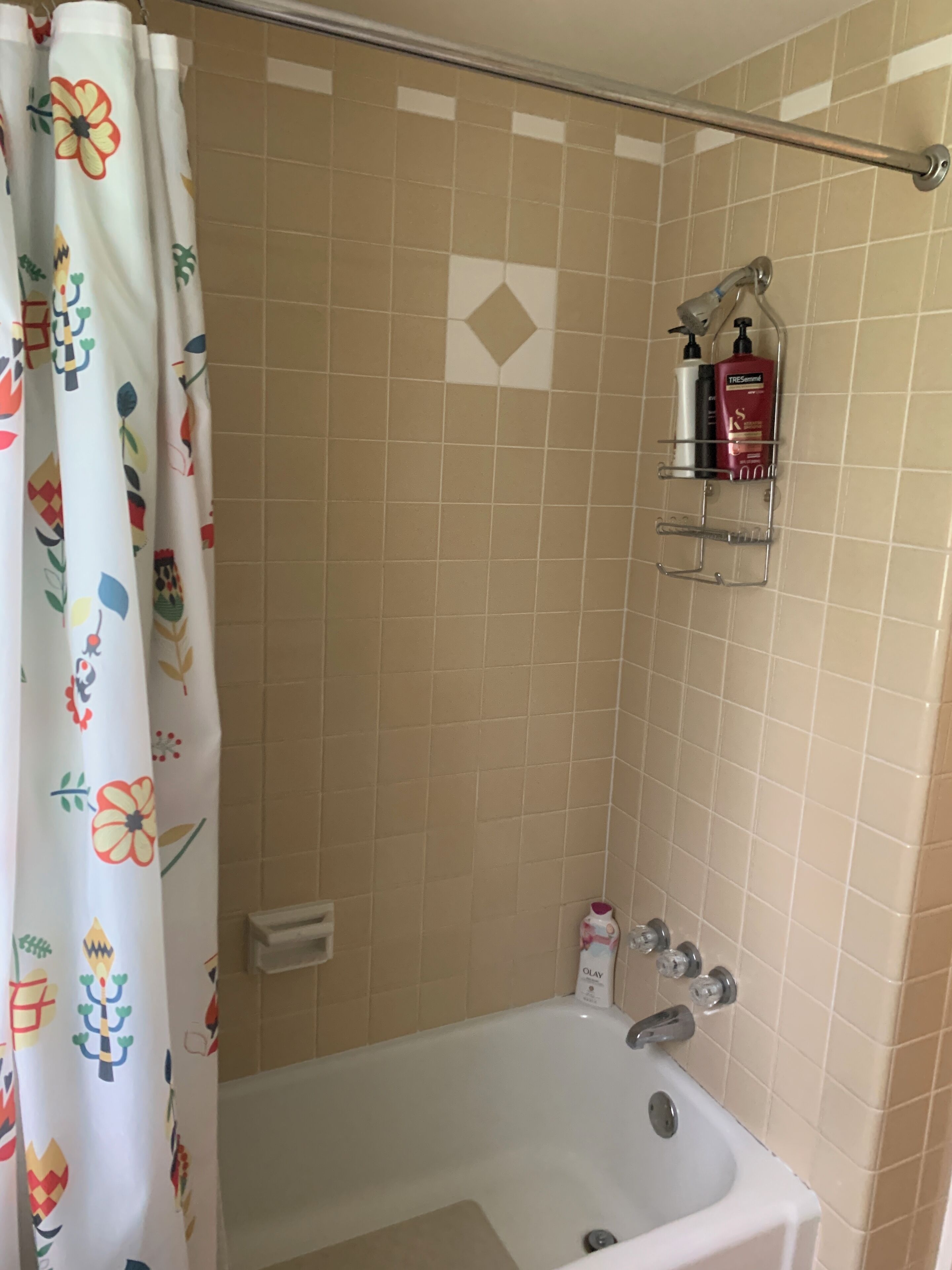 Un baño con bañera, cortina de ducha con motivos florales, un perchero y un estante con artículos de aseo.