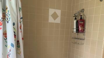 Un baño con bañera, cortina de ducha con motivos florales, un perchero y un estante con artículos de aseo.