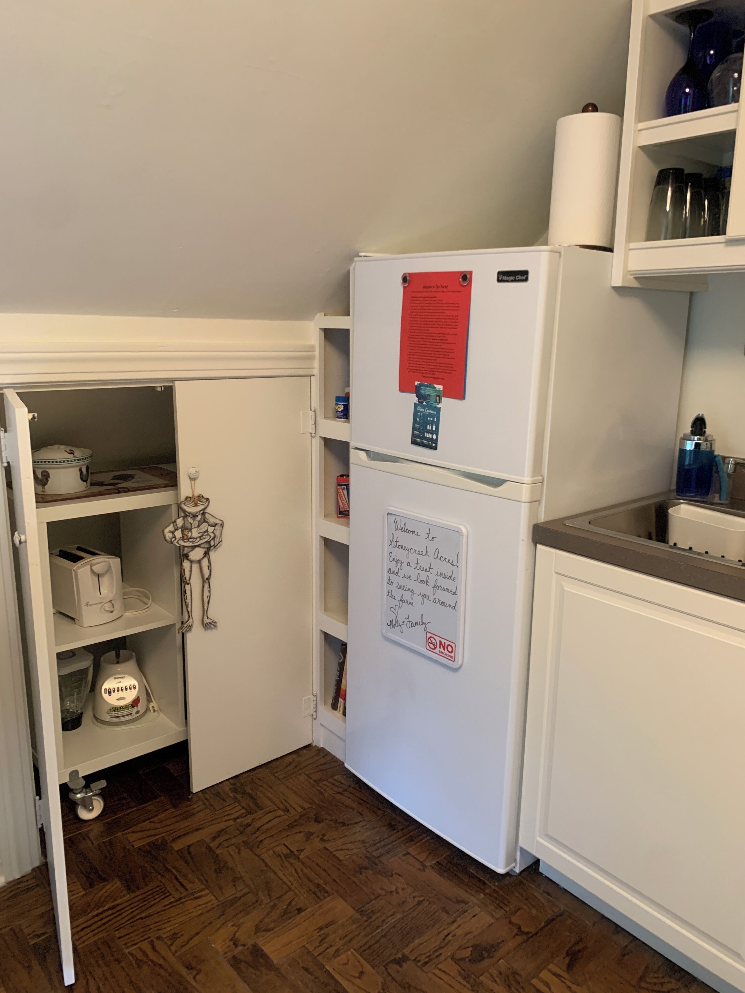 A compact kitchen with a white refrigerator, a small pantry, and a wooden floor.
