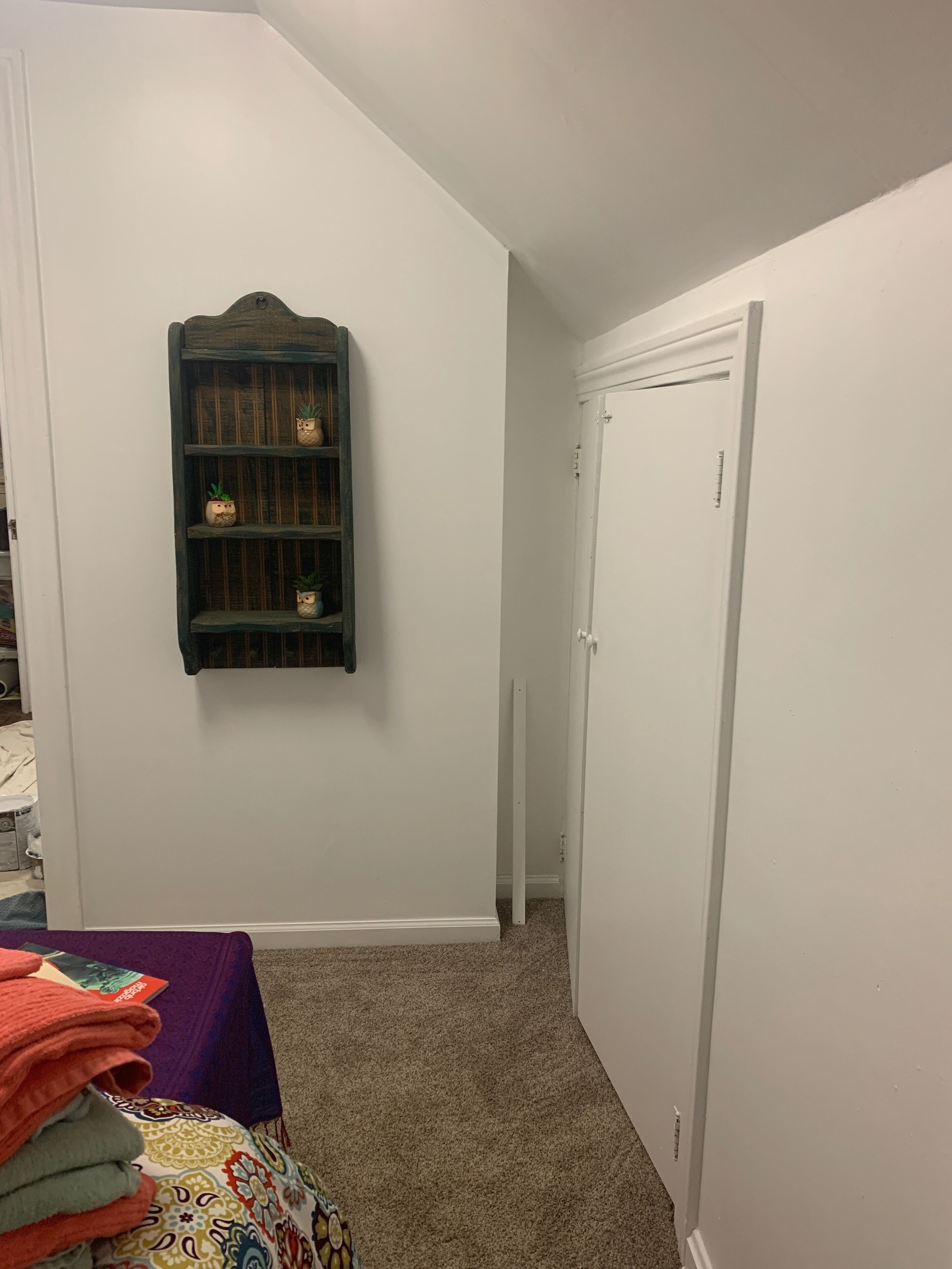 Una stanza con una porta bianca, un piccolo ripiano in legno con oggetti decorativi e un tavolo con asciugamani piegati.