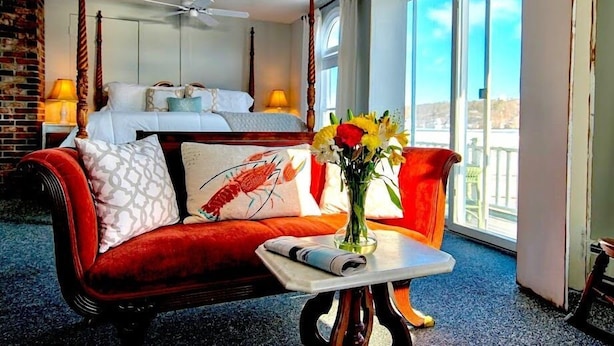 A bedroom with a four-poster bed, a red sofa, a small table with a vase of flowers, and a balcony with a view. - Captain Sawyer's Bed & Breakfast (Boothbay Harbor)