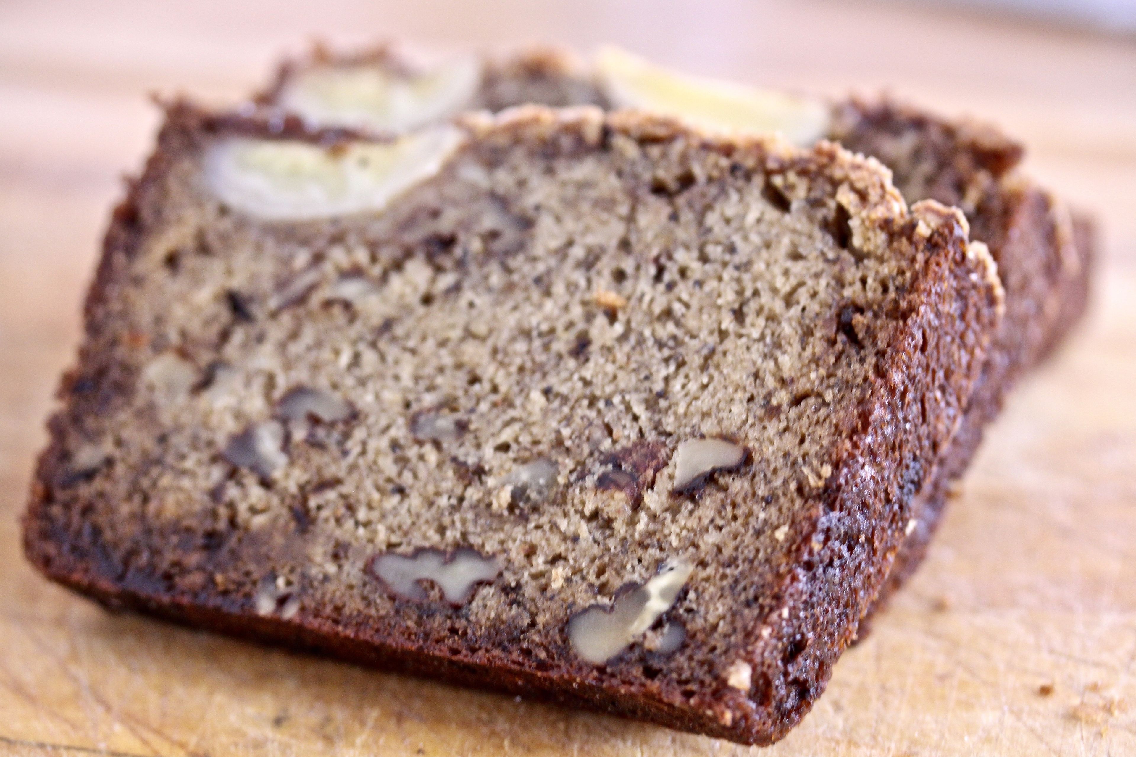 A slice of dark bread with visible nuts and seeds on a wooden surface.