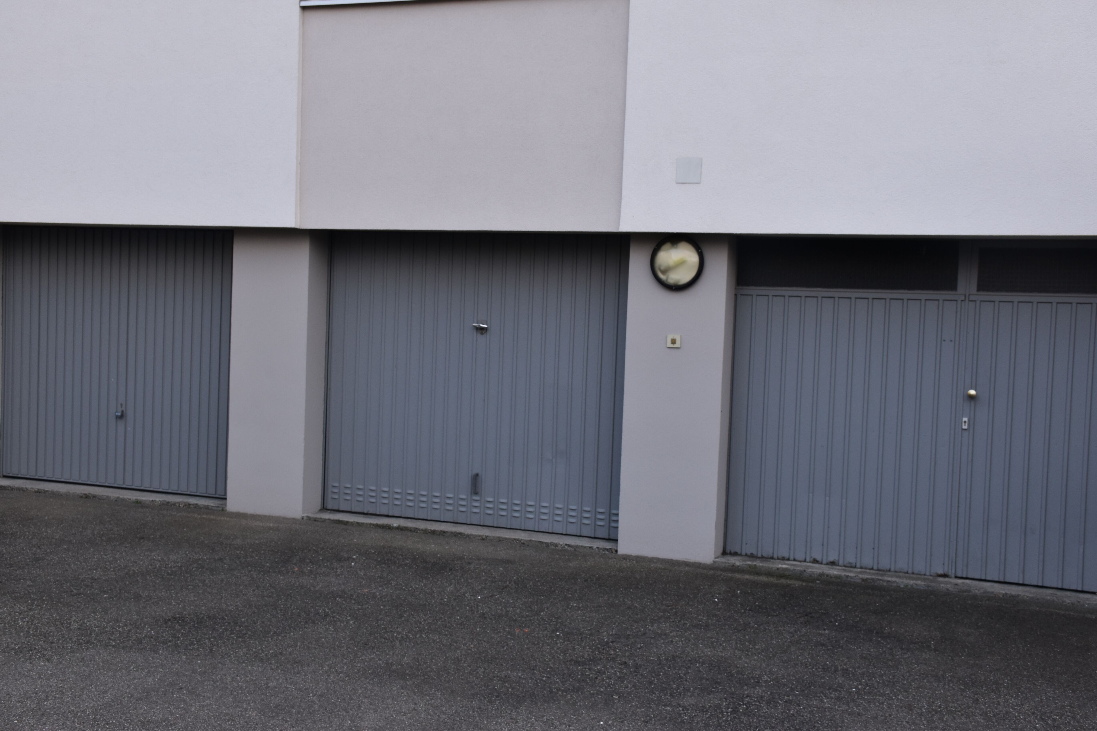 A building with three closed grey garage doors and a clock on the wall.