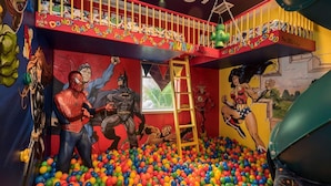 Una sala de juegos con una piscina de pelotas, murales de superhéroes y un tobogán.