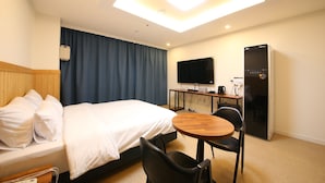Ett hotellrum med en säng, ett skrivbord med en platt-TV, ett kylskåp och en taklampa.