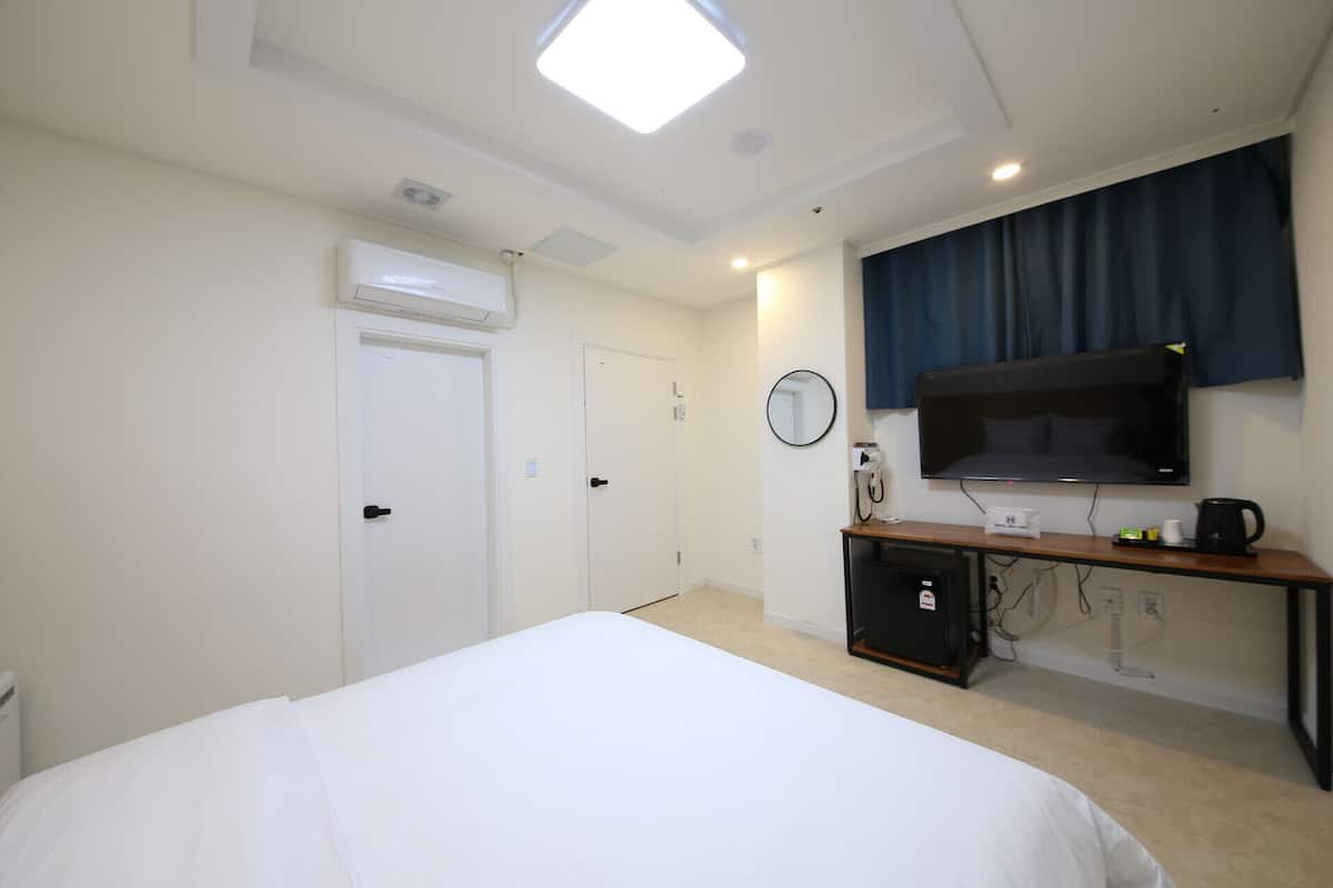 A hotel room with a bed, a TV, a desk with a computer, and a window with curtains.