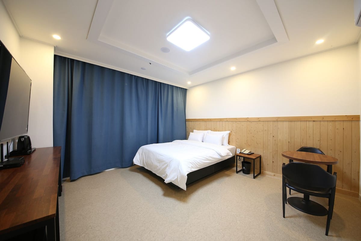 A hotel room with a bed, a desk with a telephone, a chair, and a small table.