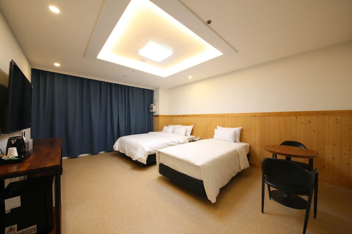 A hotel room with two beds, a desk, a chair, and a television.