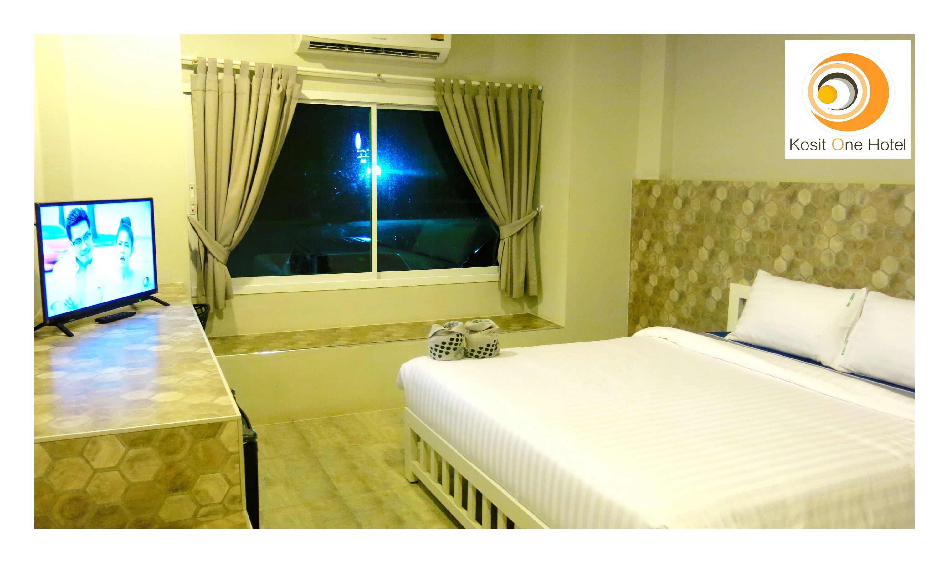 A hotel room with a bed, a TV, a window with curtains, and a view of the night sky.