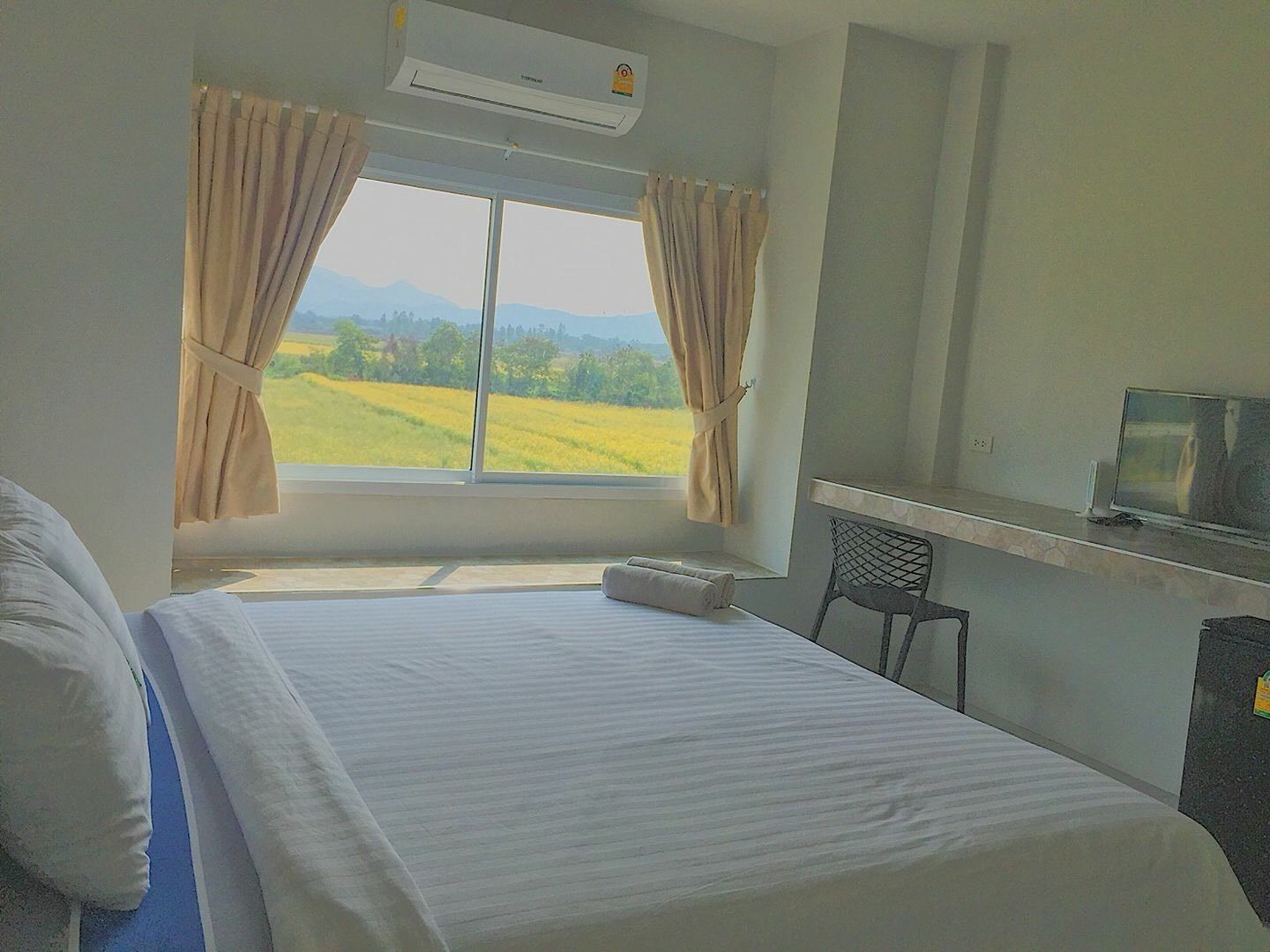Een hotelkamer met een bed, een televisie en een raam met gordijnen.