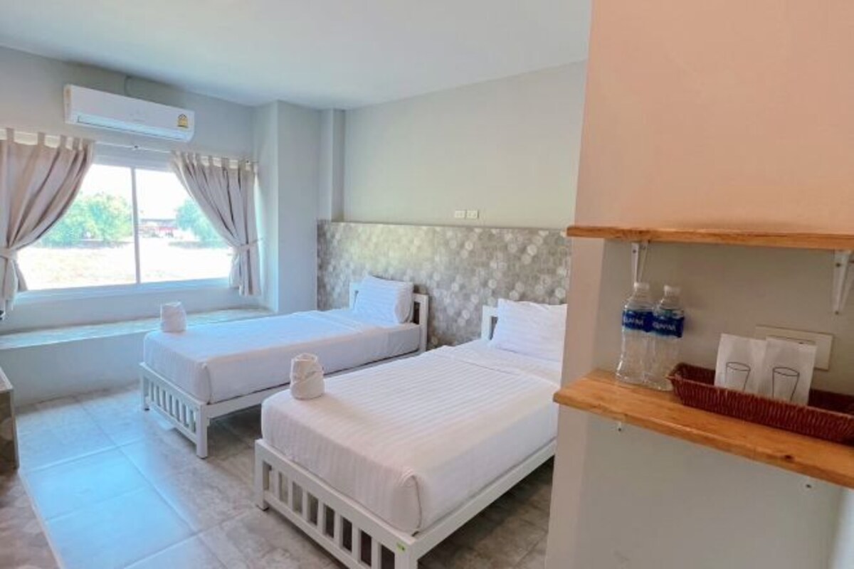 A hotel room with two beds, a window with curtains, a wooden shelf with toiletries, and a tiled floor.