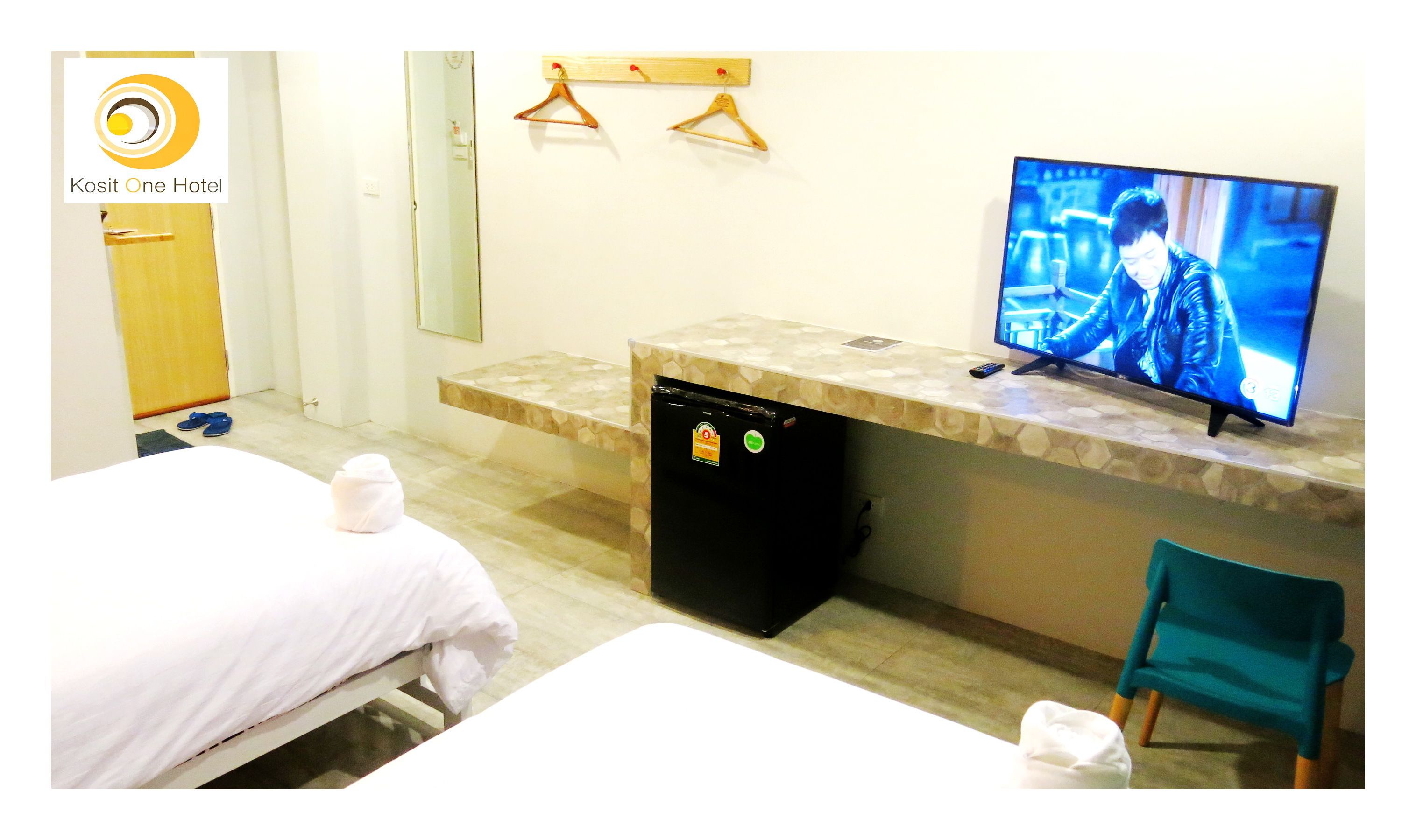 A hotel room with a bed, a small desk with a television, a chair, and a refrigerator.
