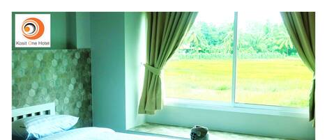 A hotel room with a bed, a window with curtains, and a view of a green landscape.