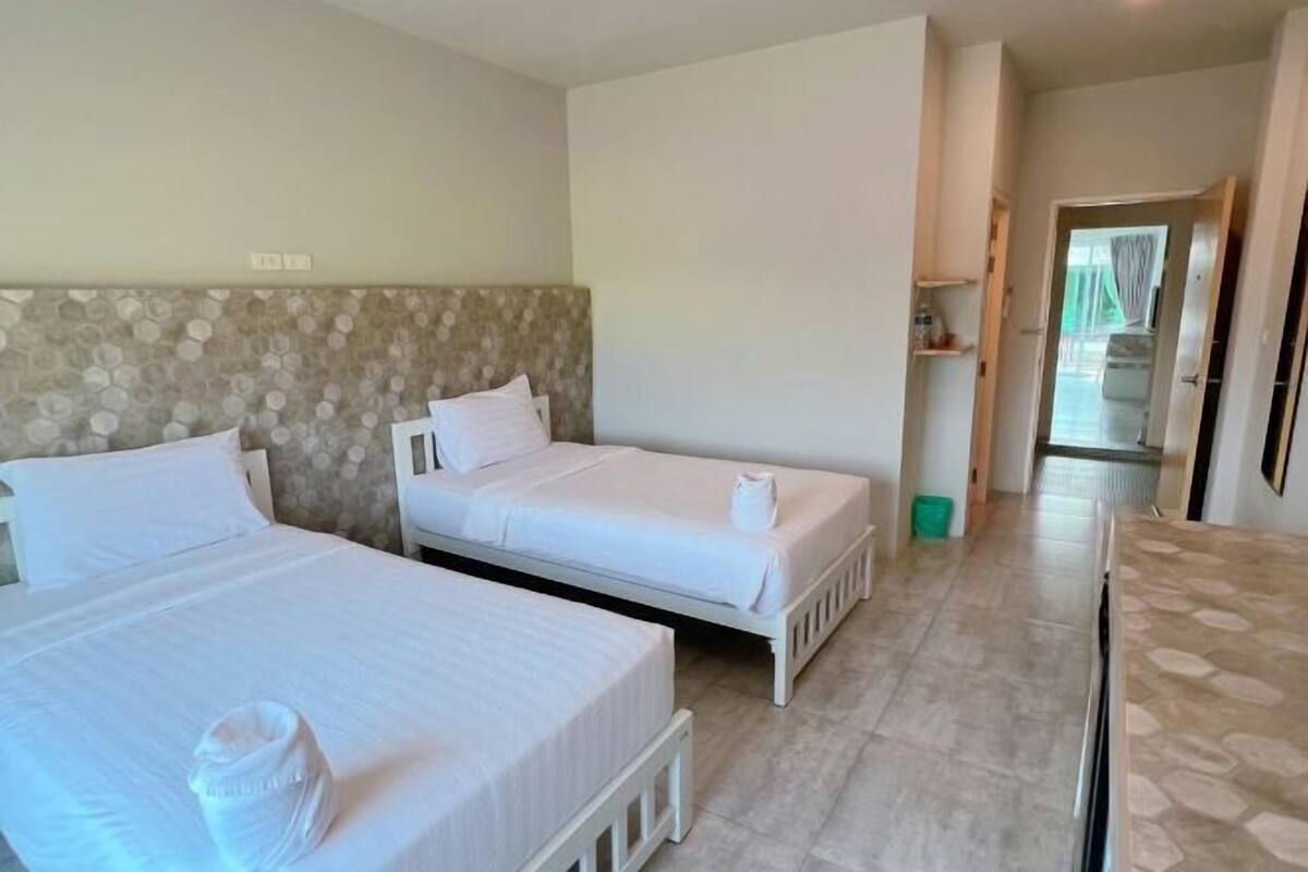 A hotel room with two beds, a stone-patterned headboard, a tiled floor, and a view of the hallway.